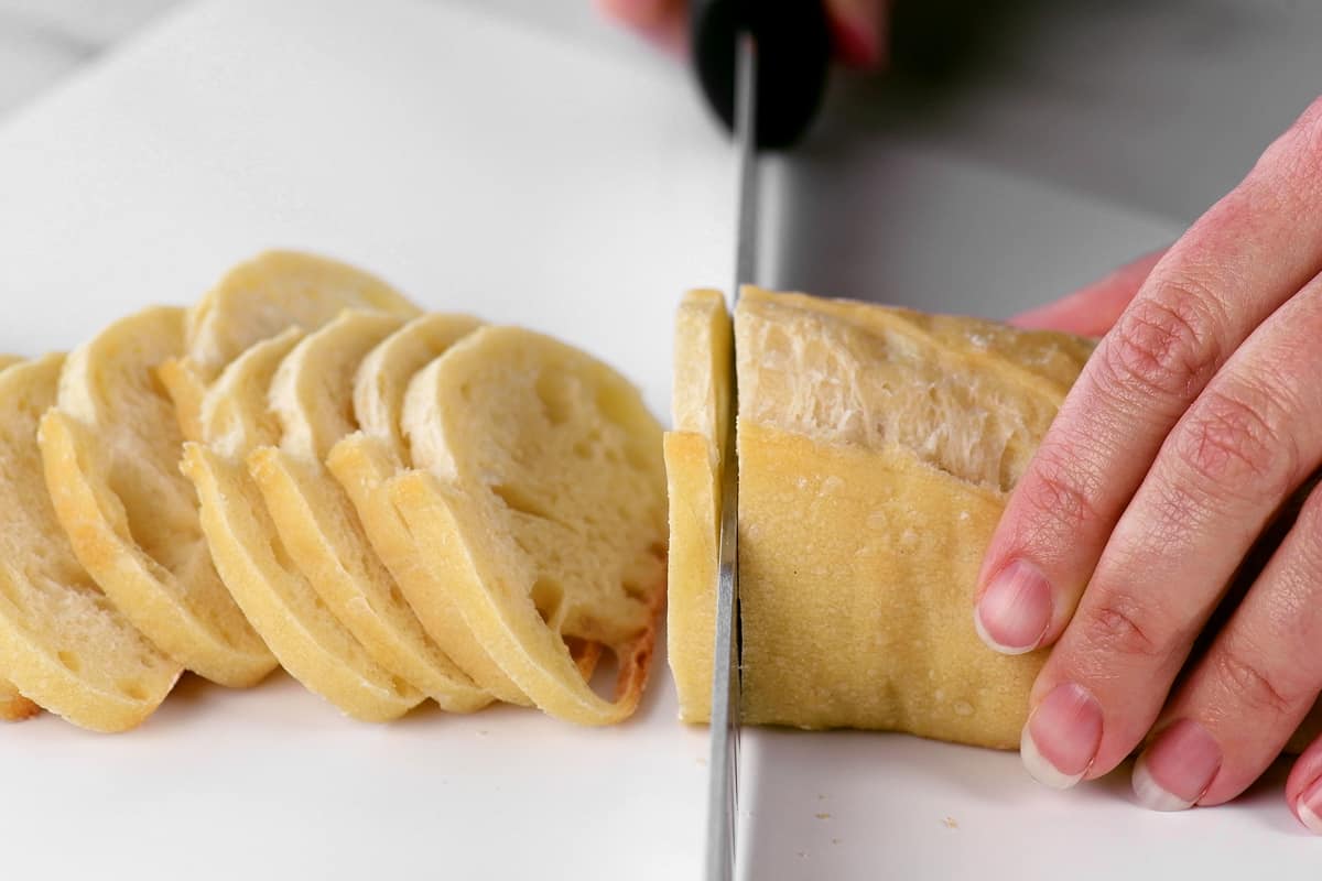 hands using a knife to cut a bread loaf into slices.