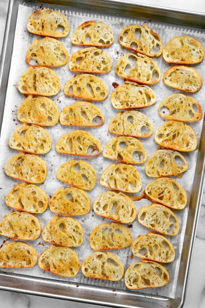 thirty-six slices of crostini bread on a baking pan.