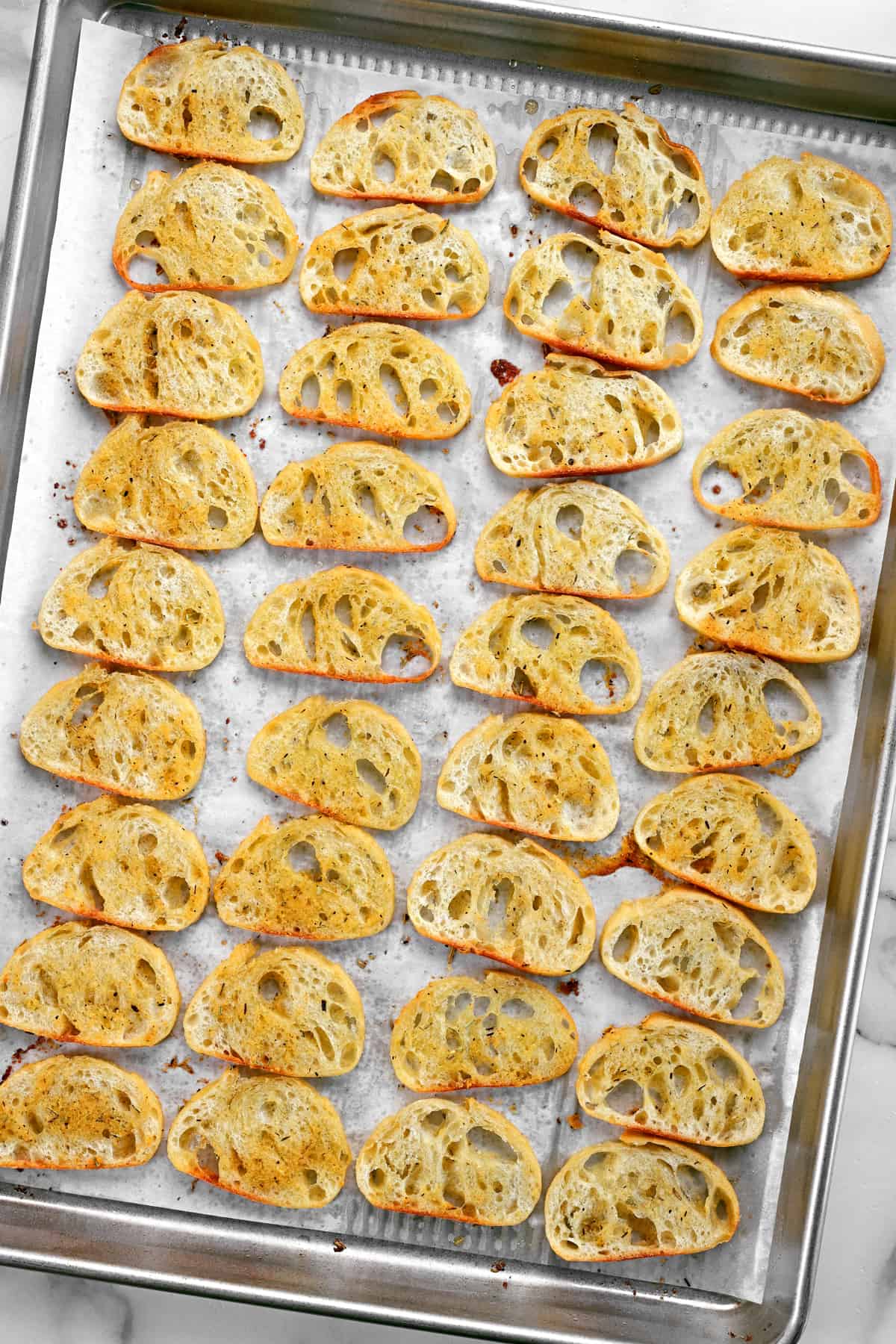 thirty-six slices of crostini bread on a baking pan.