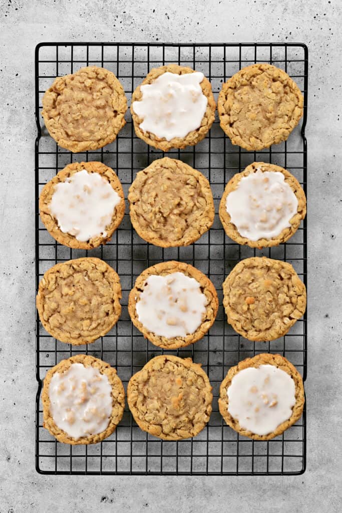 a dozen oatmeal cookies and iced oatmeal cookies on a wire rack.