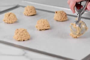 a cookie dough scoop adding a ball of dough to a parchment lined baking sheet.