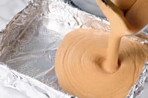 pouring the melted peanut butter fudge into a foil lined pan.