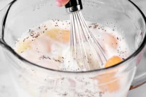 a hand using a whisk to stir the sausage egg bake ingredients.