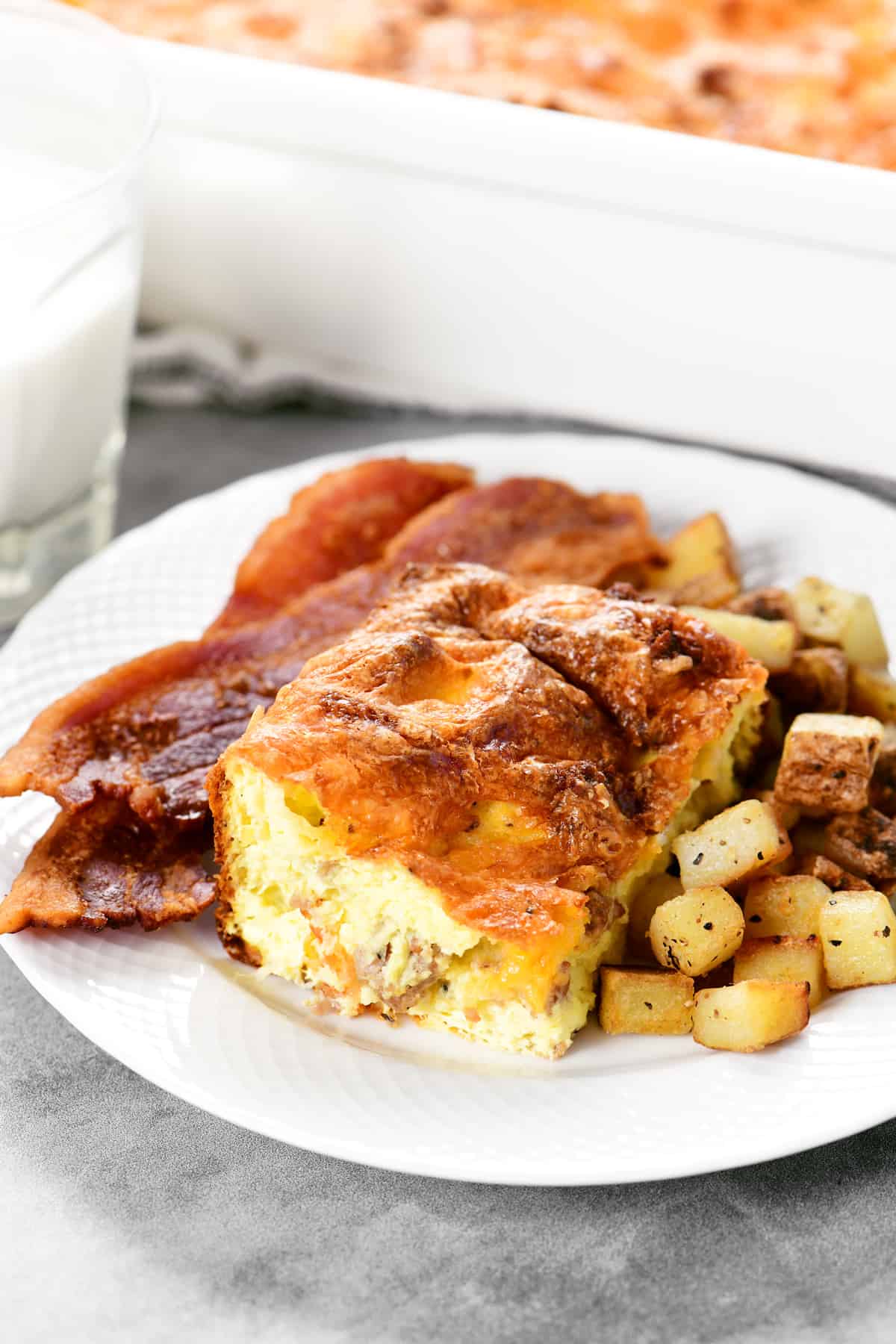 breakfast casserole on a plate with potatoes and bacon.