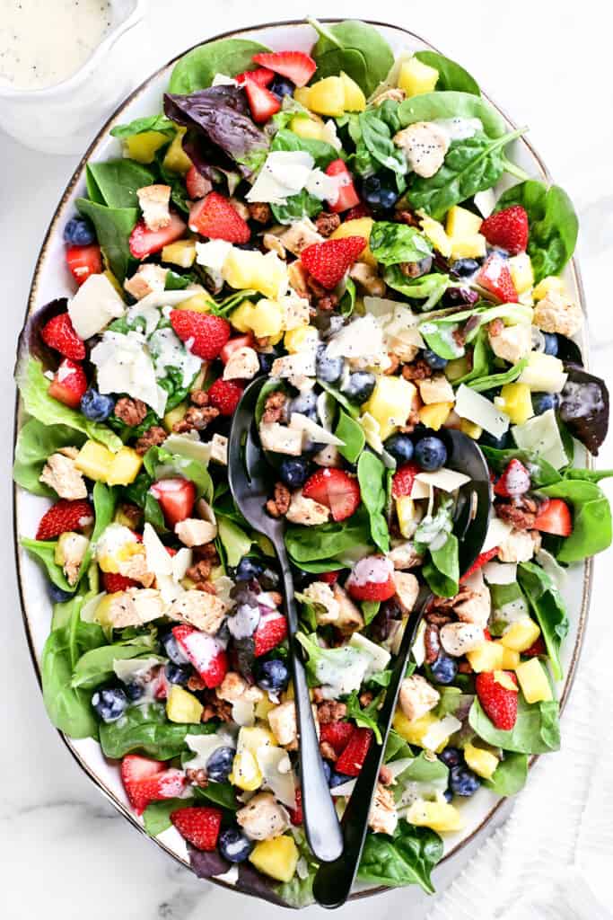 strawberry spinach salad in a bowl with salad tongs.