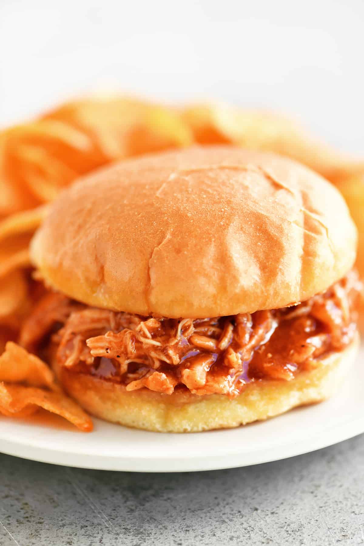 bbq chicken sandwich on a white plate with chips.