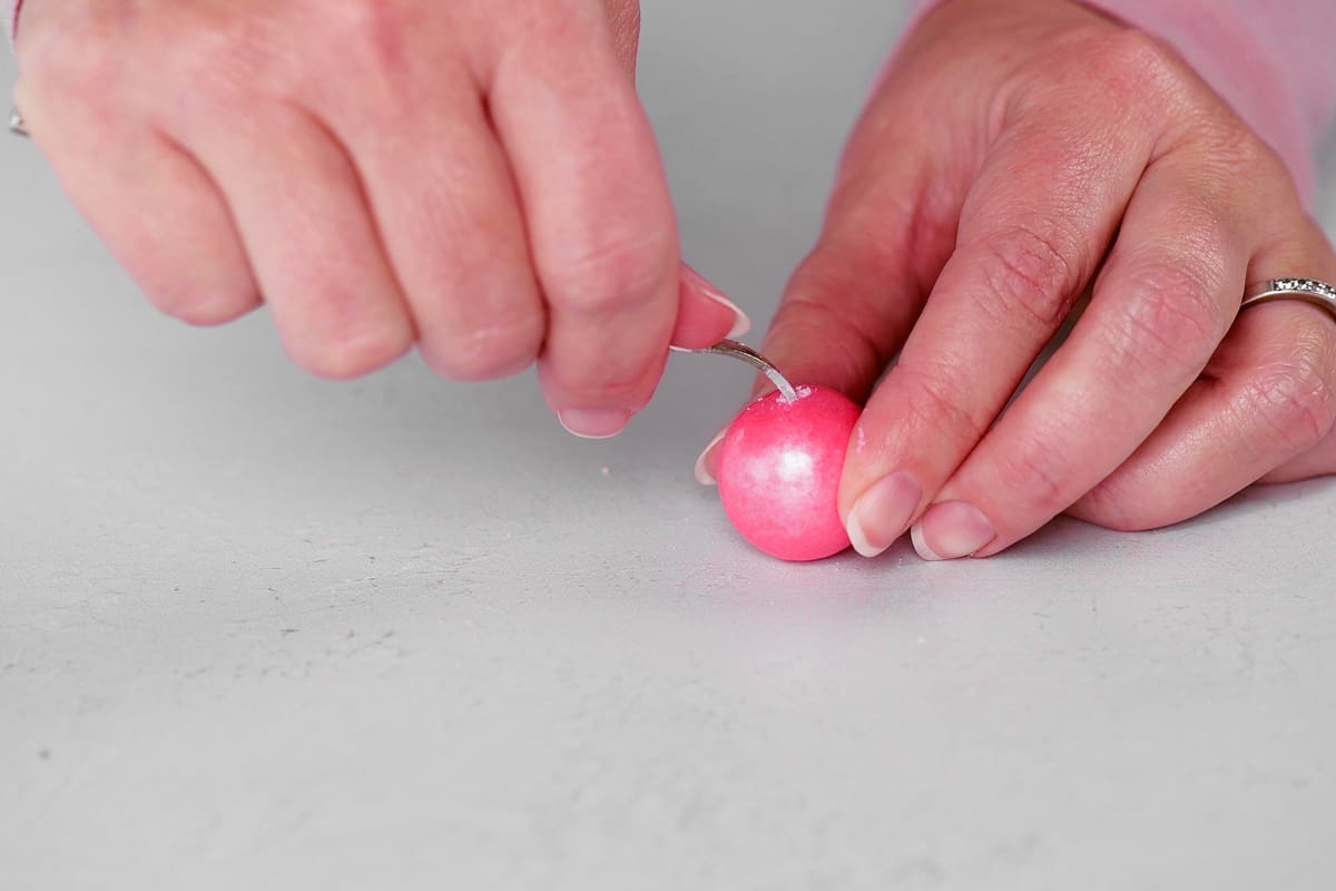 hands using a nut pick to poke a hole in a pink gumball.
