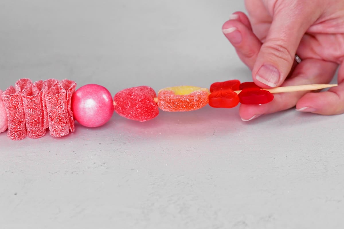 a hand sliding a red butterfly shaped gummy candy on to a kabob stick.