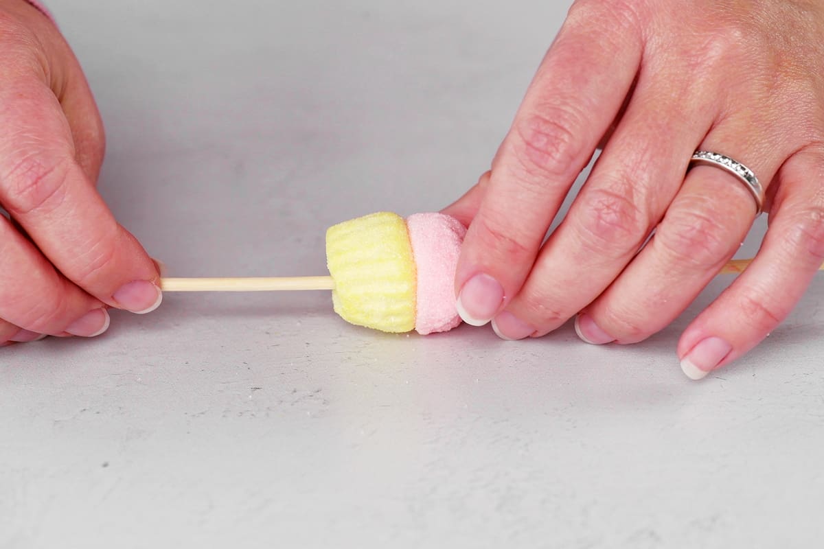 hands sliding a marshmallow cupcake on to a wooden stick.