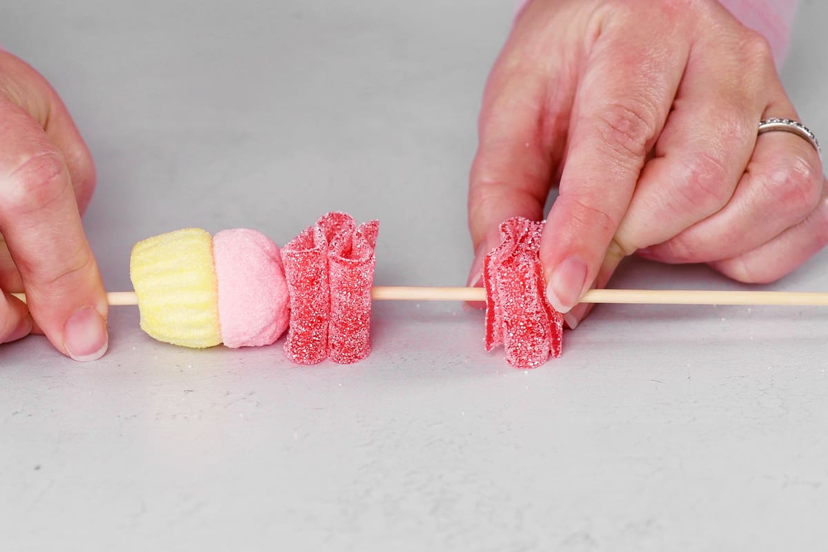 hands sliding folded sour belt candies on to a wood stick.