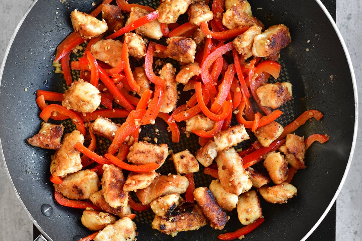 cubed chicken and sliced red peppers in a frying pan.