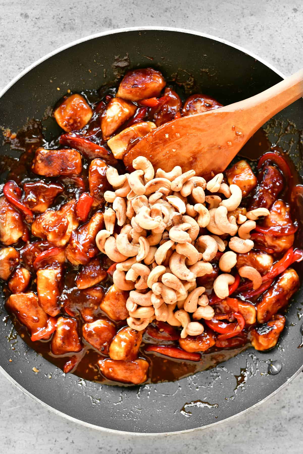 a frying pan with chicken, sauce and cashews inside.