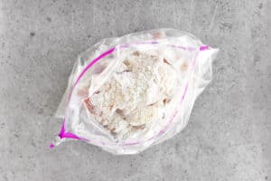 uncooked chicken coated in flour inside of a plastic zip-top bag.