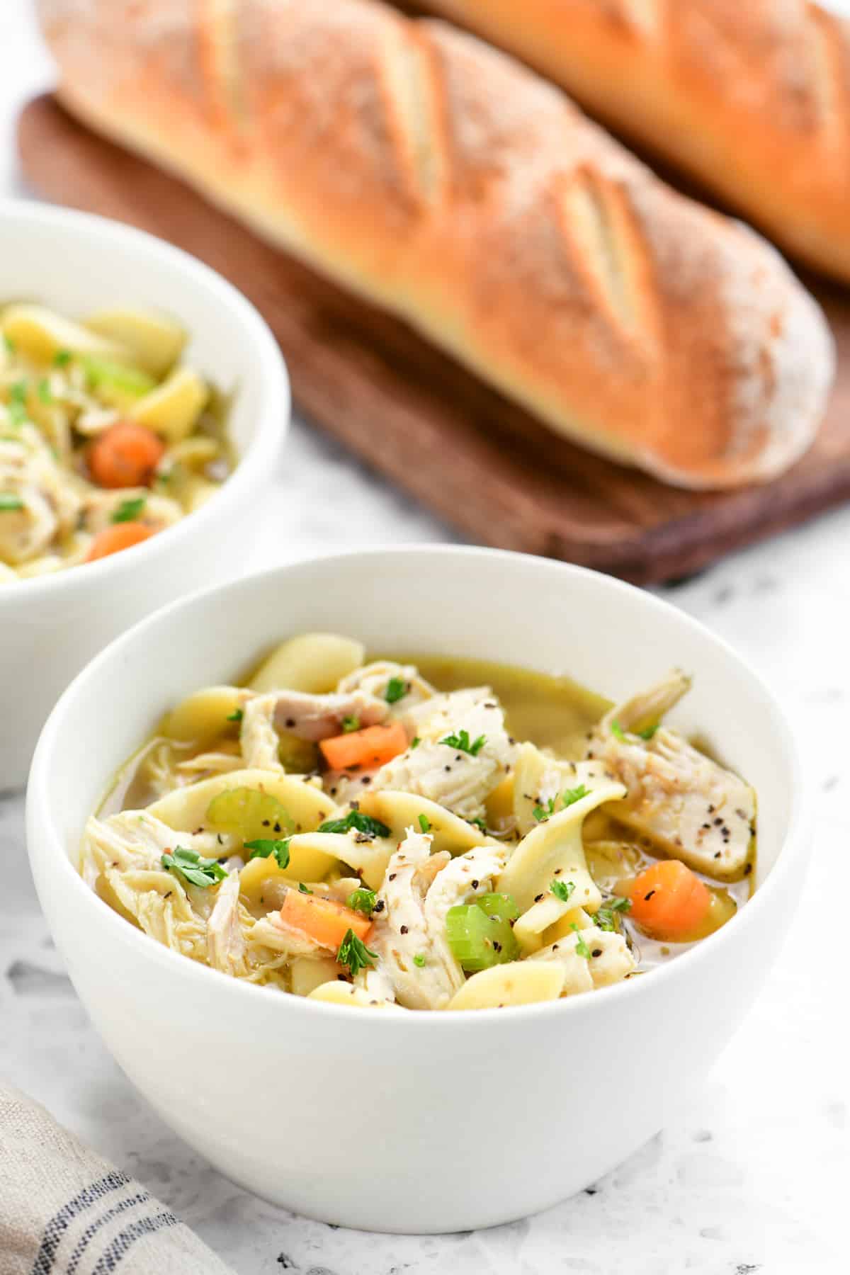chicken noodle soup in bowls with two loaves of bread in the background.