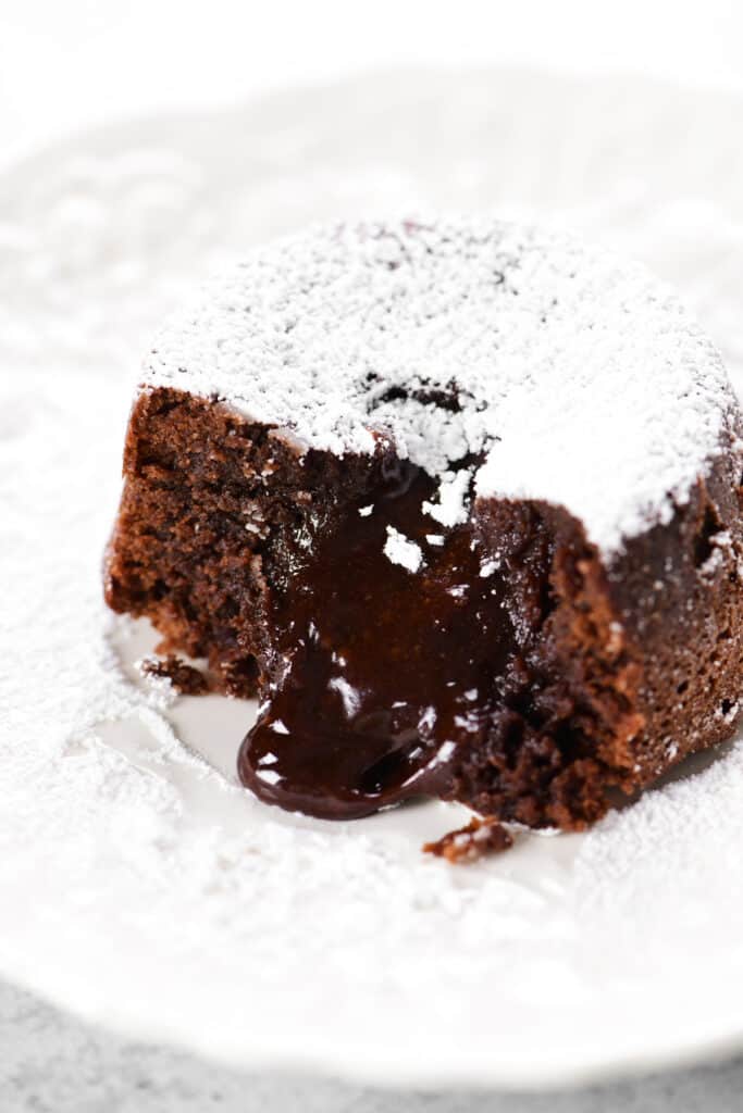 molten chocolate filling oozes out of a lava cake on a plate.