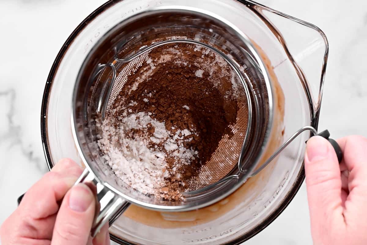 hands using a sifter to sift cocoa powder.