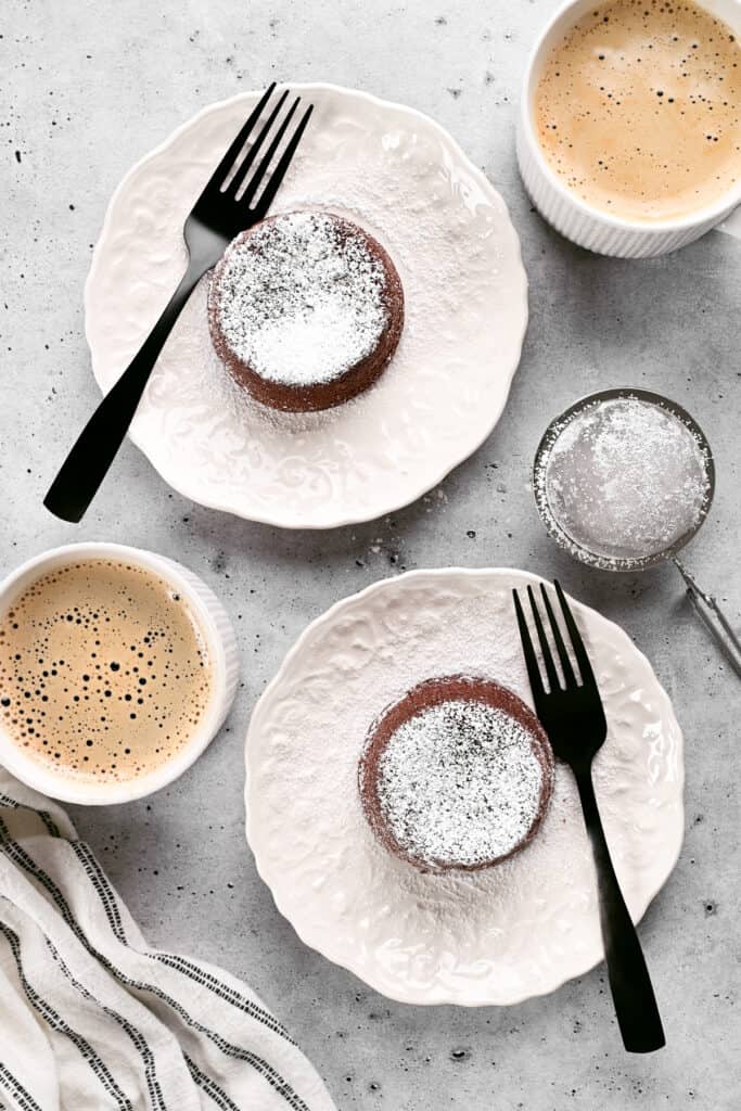 lava cakes on plates with two cups of coffee on a countertop.