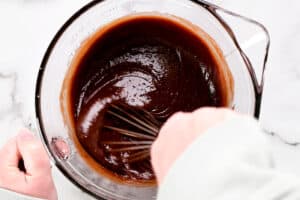 hands using a whisk to stir cake ingredients.