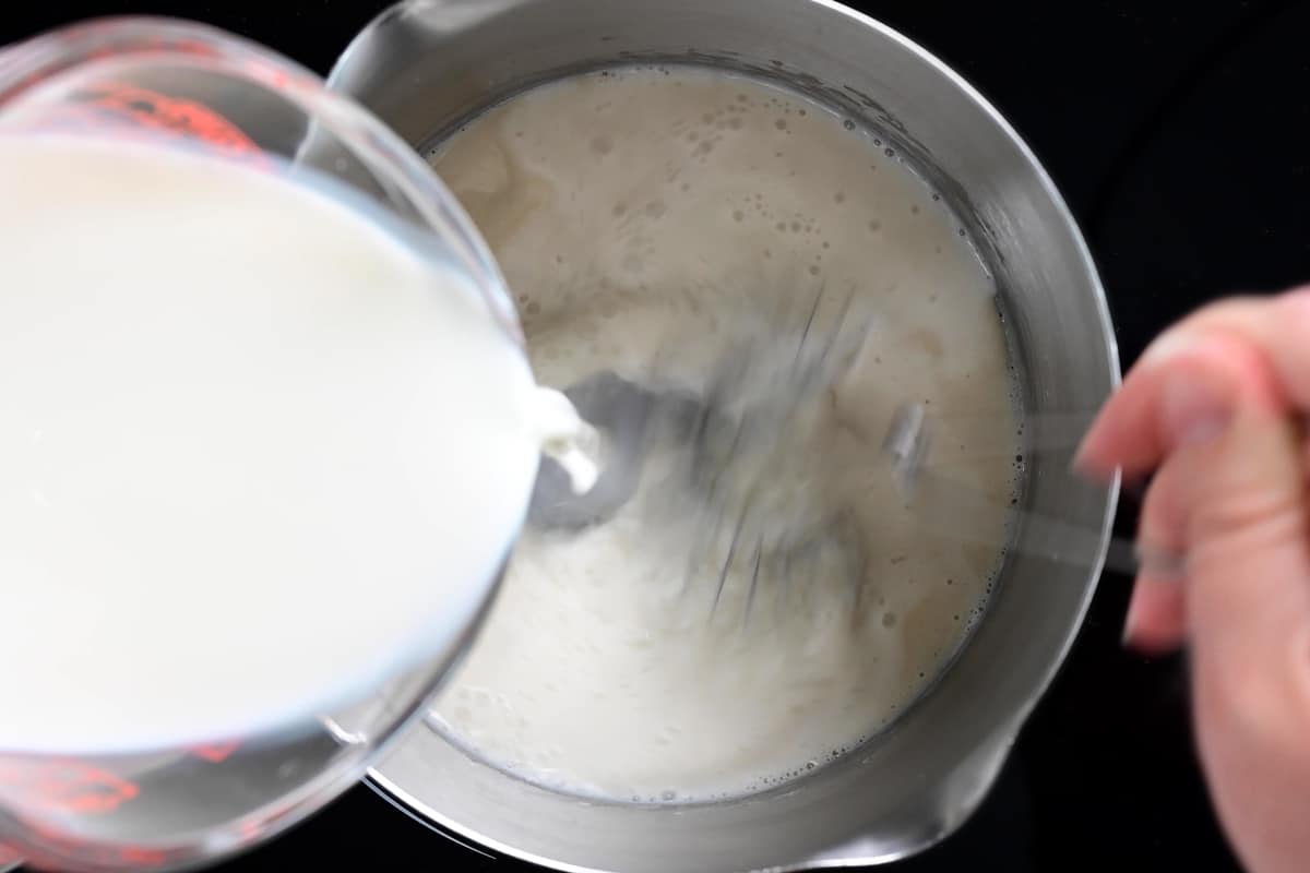 whisking milk into the roux in a saucepan.