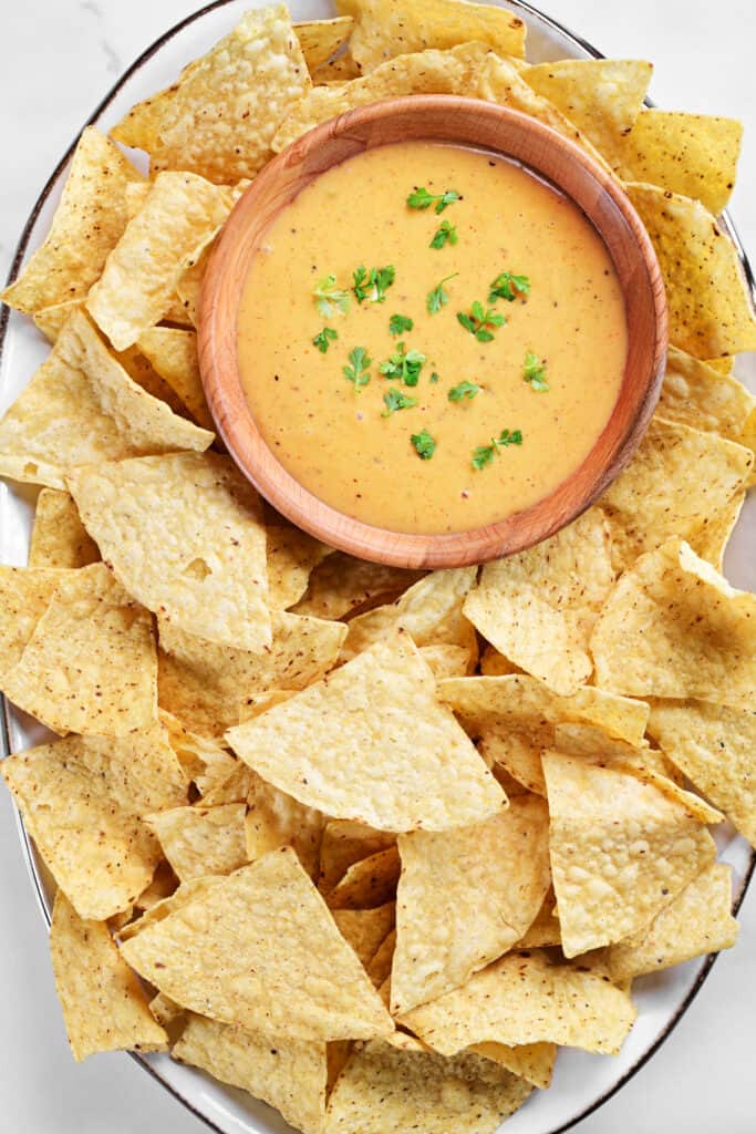 a white tray full of tortilla chips surrounding a bowl of nacho cheese sauce.