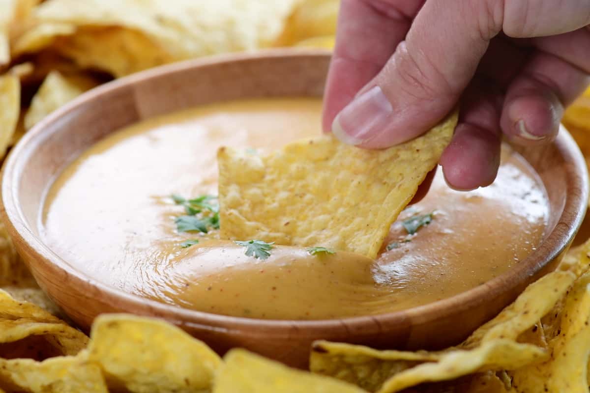 scooping nacho cheese, from a wooden bowl, with a tortilla chip.