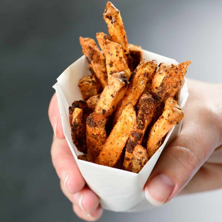 a hand holding nacho fries in a paper cup.