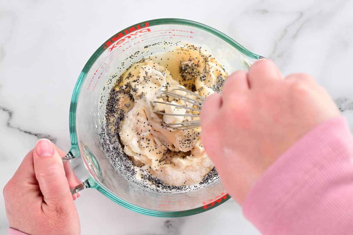 a hand whisking ingredients in a small glass bowl.