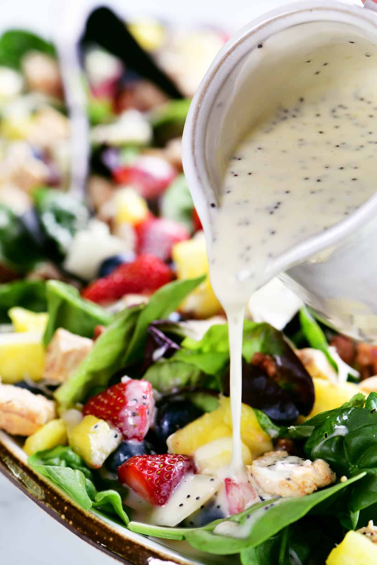 pouring poppy seed dressing from a white pitcher onto a salad.