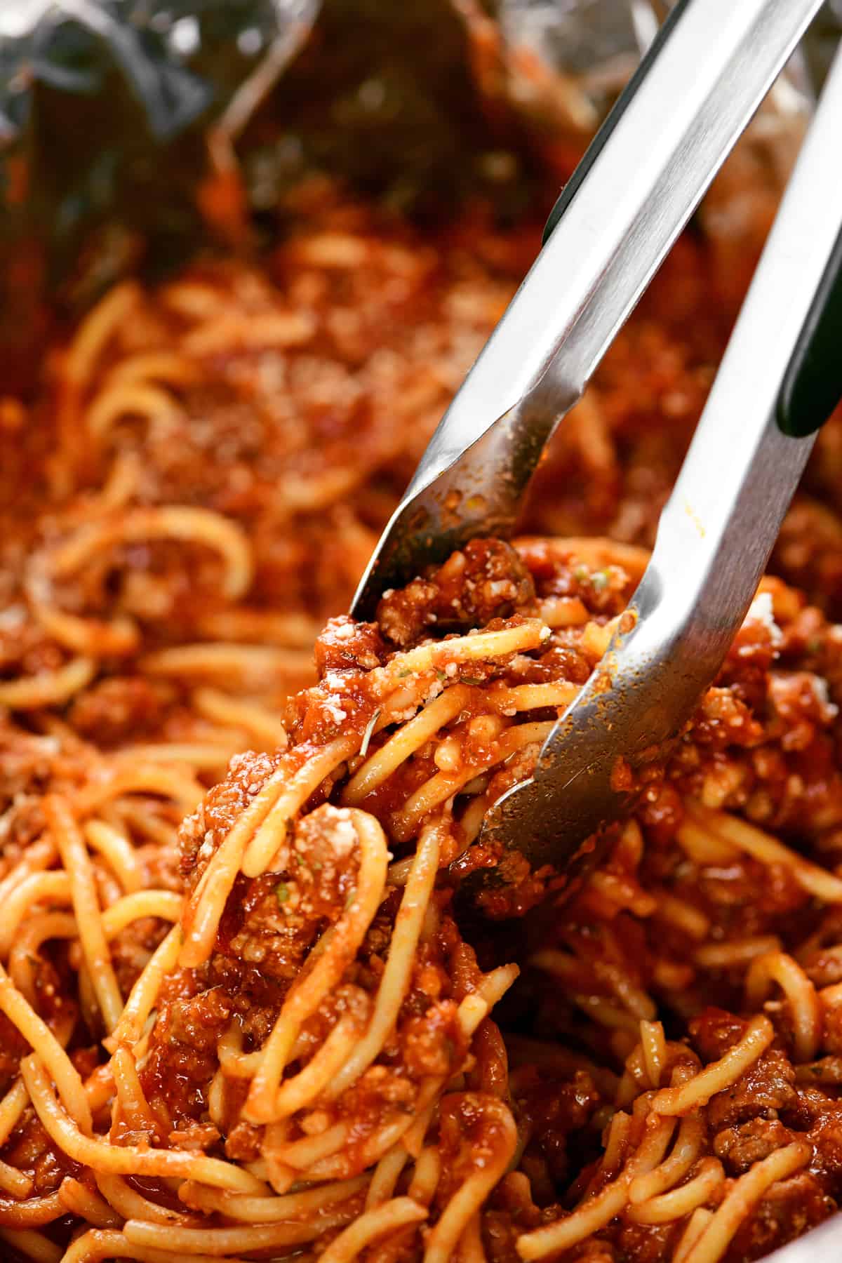 tongs scooping crock pot spaghetti.