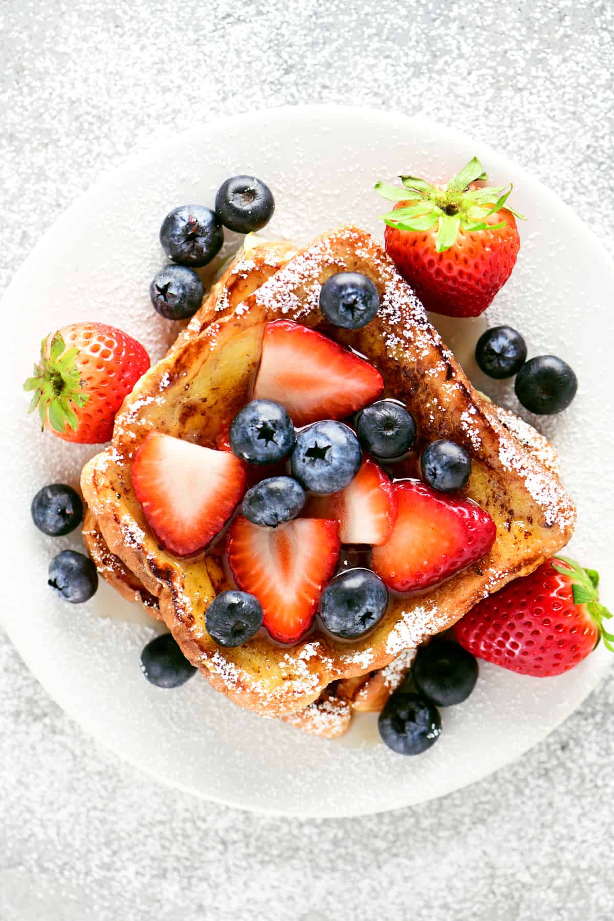Two slices of french toast with blueberries and strawberries on a plate.