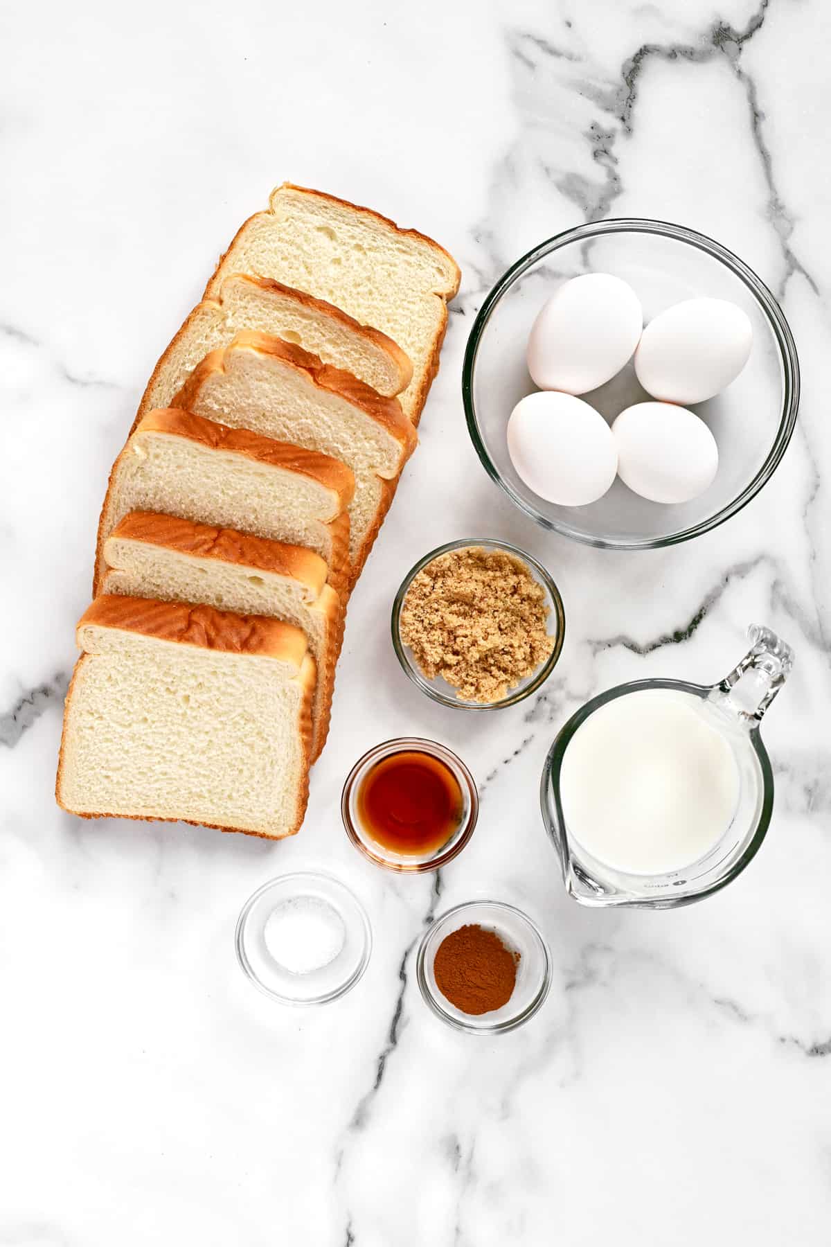 Sliced bread, eggs, and other ingredients on a white marble countertop.