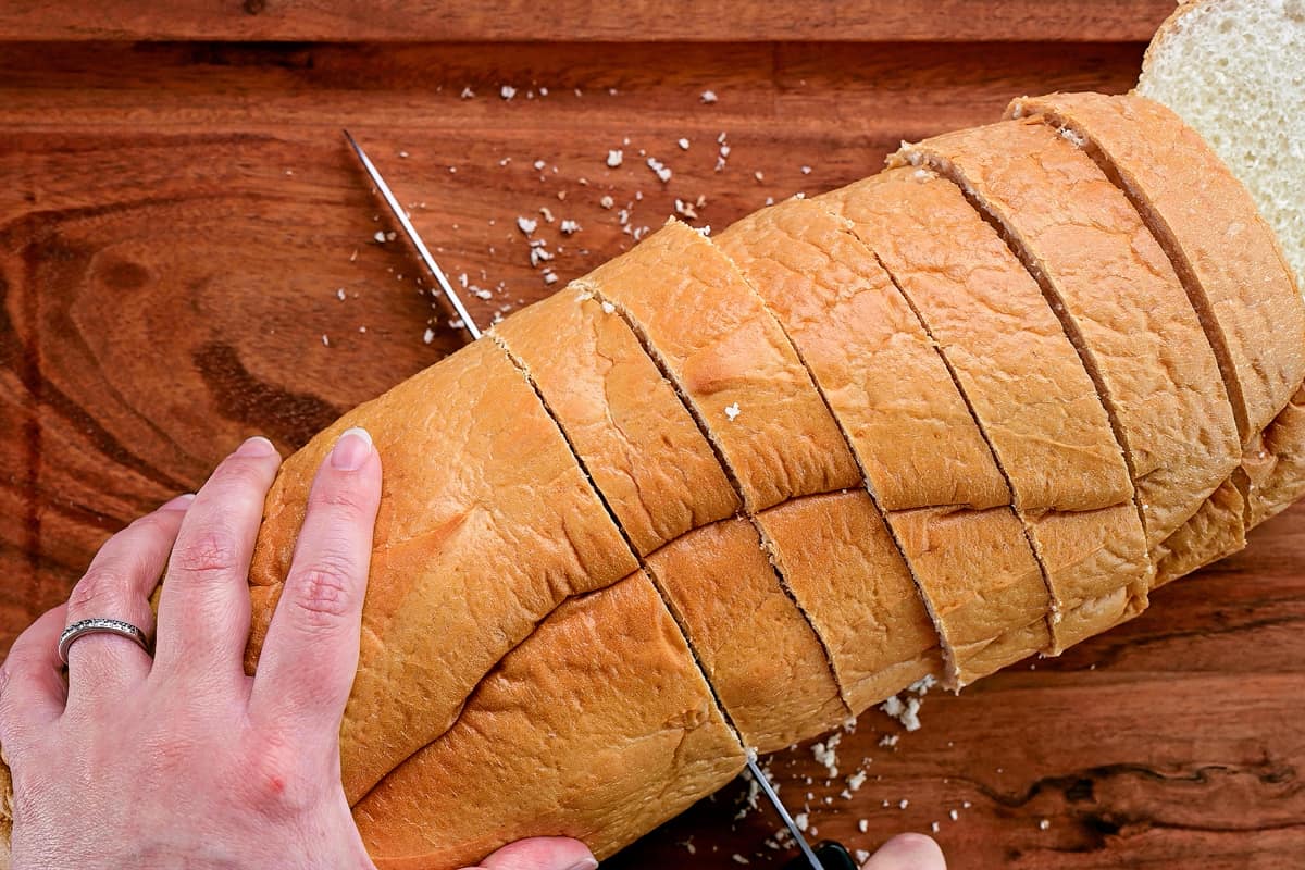 Hands using a knife to slice bread.