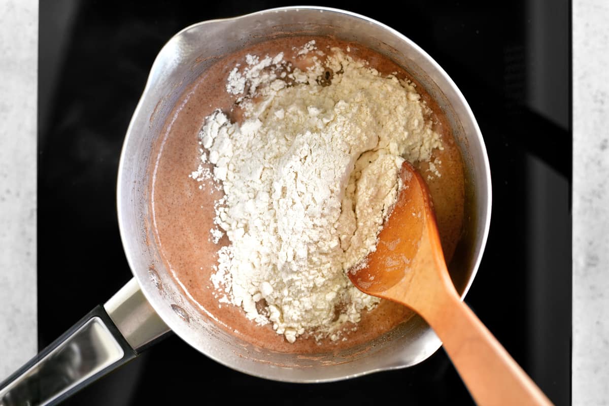 A wooden spoon and flour in dough mixture, which is in a kettle.