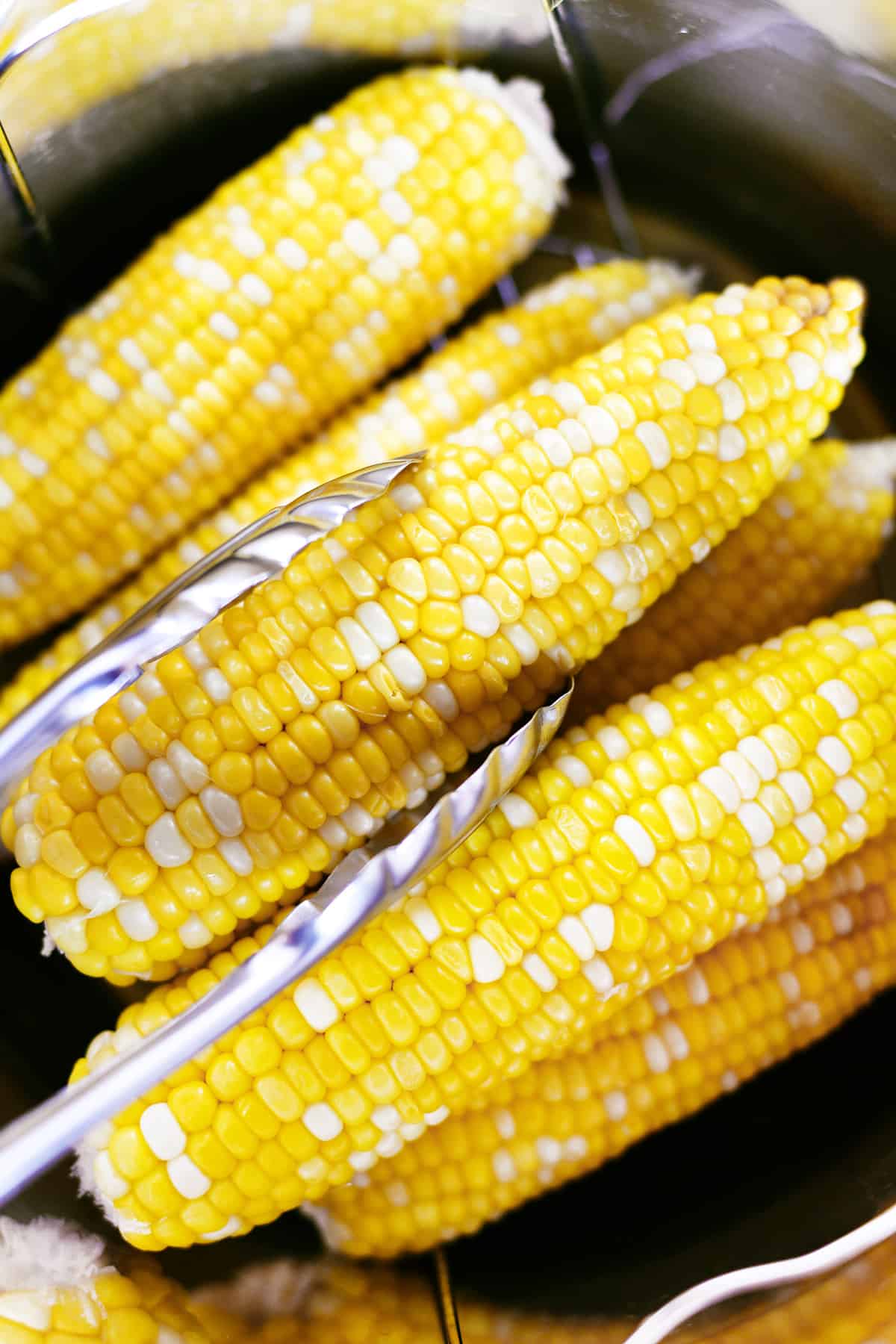 Tongs removing corn on the cob from an instant pot.