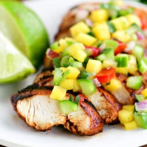 Mango chicken topped with mango salsa on a white plate.