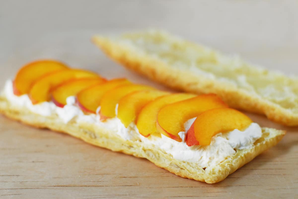 Sliced peaches on whipped cream and napoleon pastry.