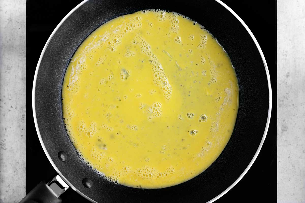 Whisked eggs spread out in a skillet.