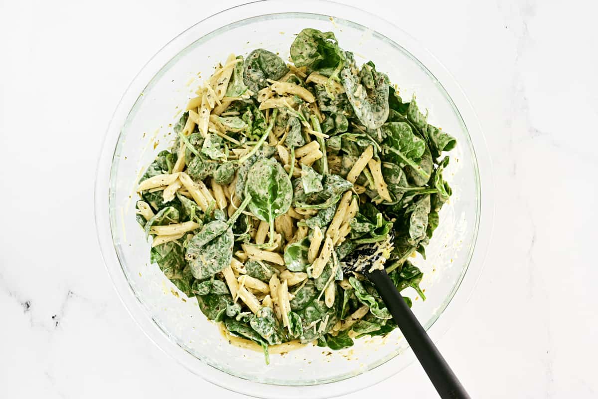 Stirring spinach pasta salad with a black spoon.