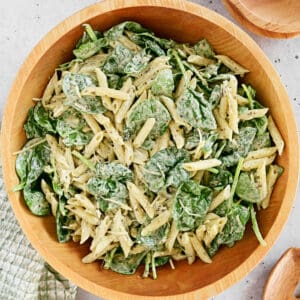 A spinach pasta salad in a wooden bowl.