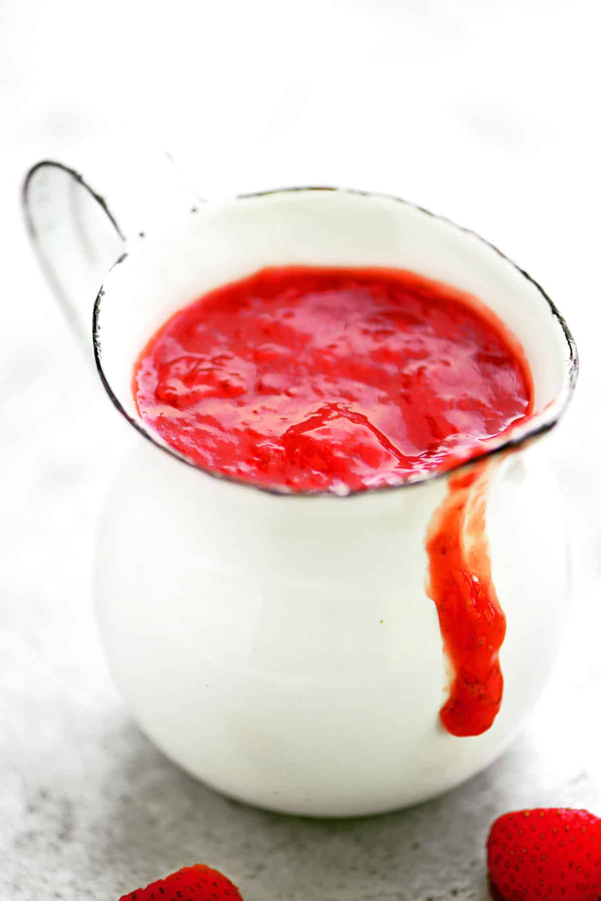 A small white pitcher with strawberry sauce inside.