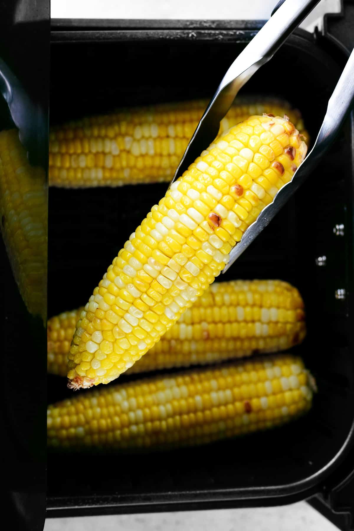 Air fryer corn on the cob being lifted by tongs.