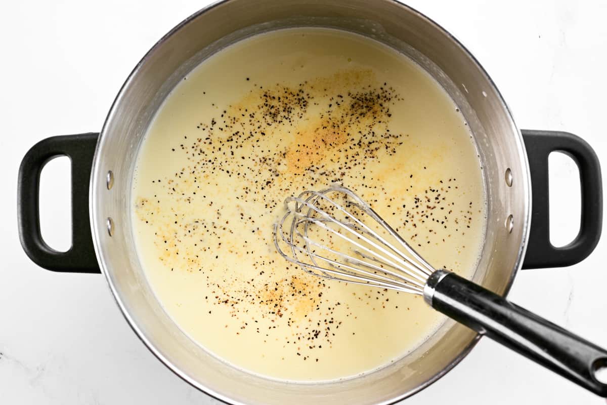 A whisk in a sauce pan with alfredo ingredients.