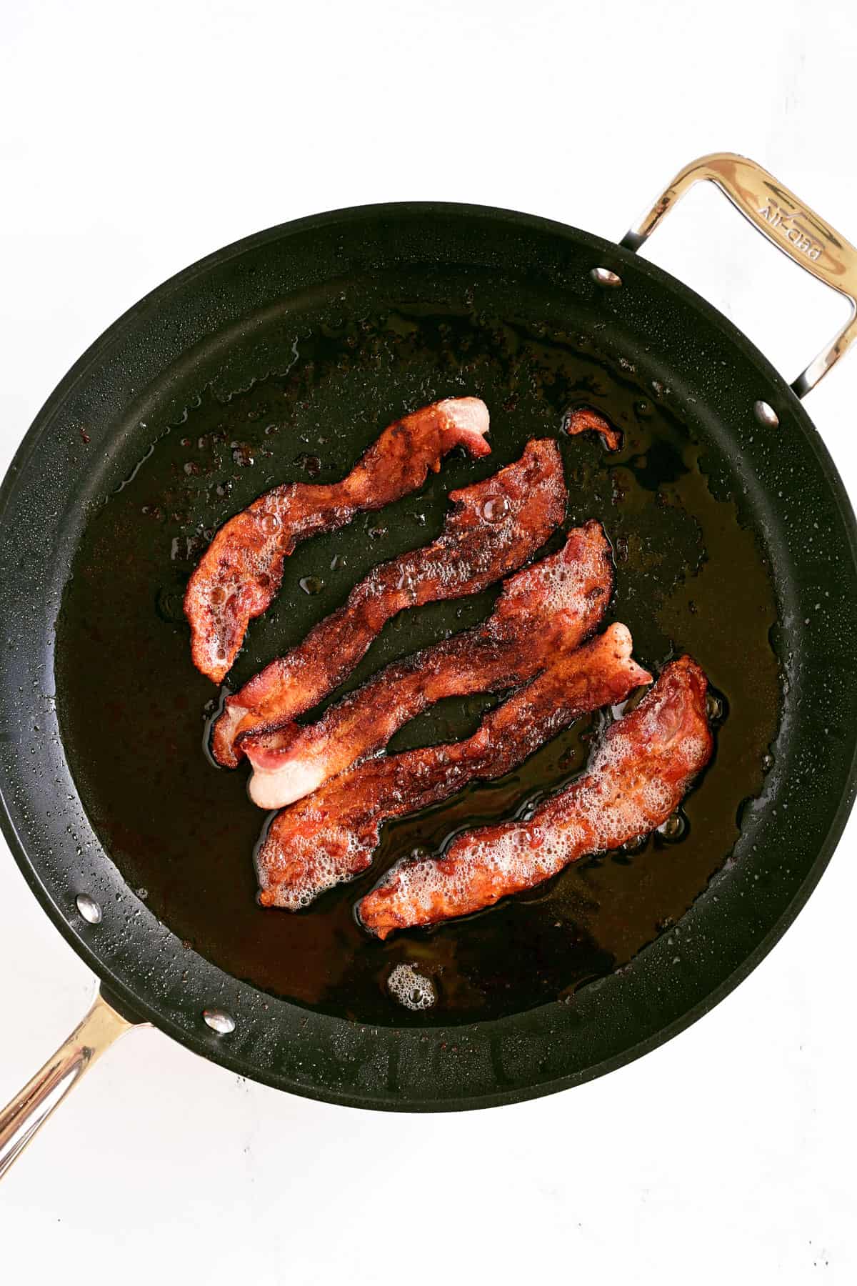 Five pieces of cooked bacon in a frying pan.