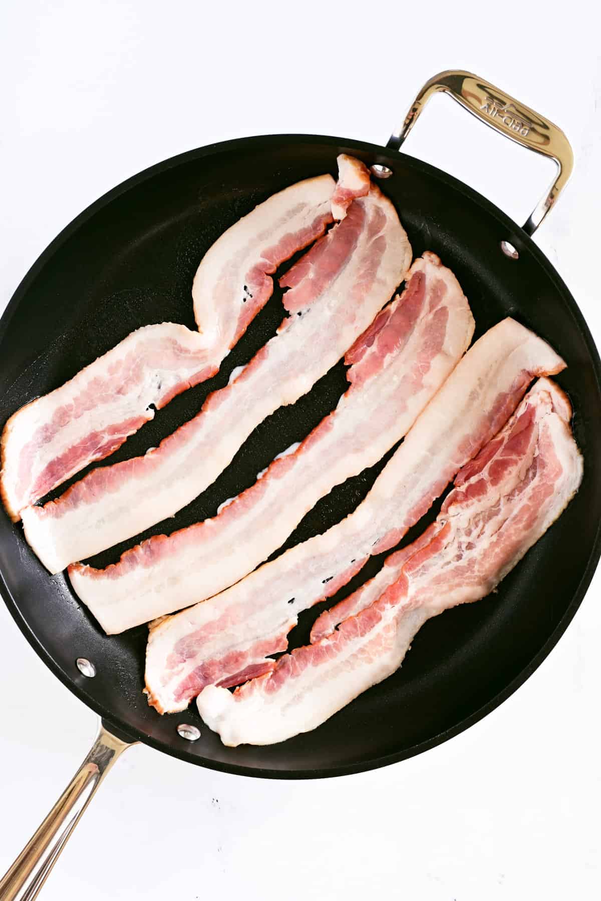 Five strips of uncooked bacon in a frying pan.