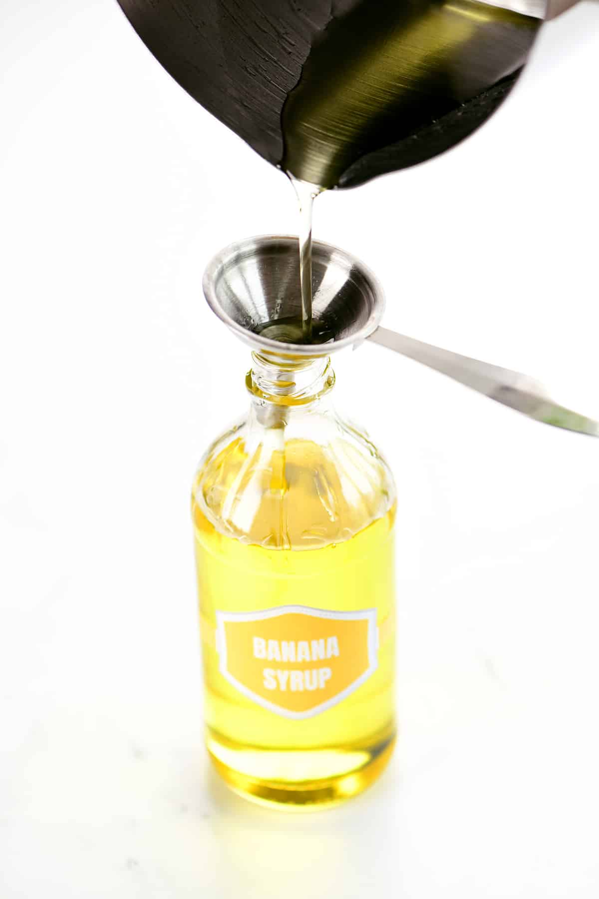 Pouring cooled banana syrup into a bottle.