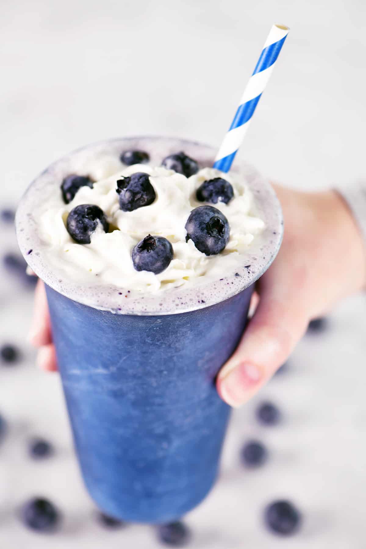A hand holding a blueberry milkshake.