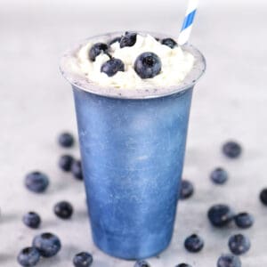 A blueberry milkshake in a blue metal glass.