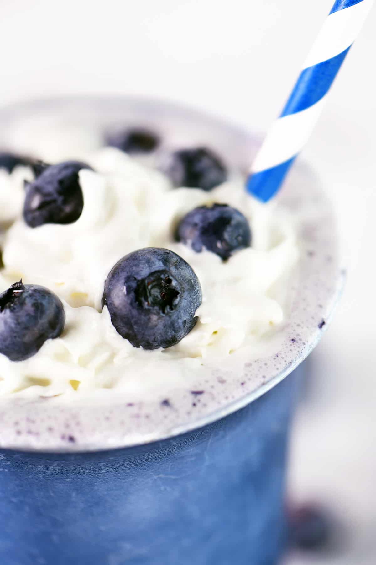 Close up of a blueberry milkshake in a blue cup.