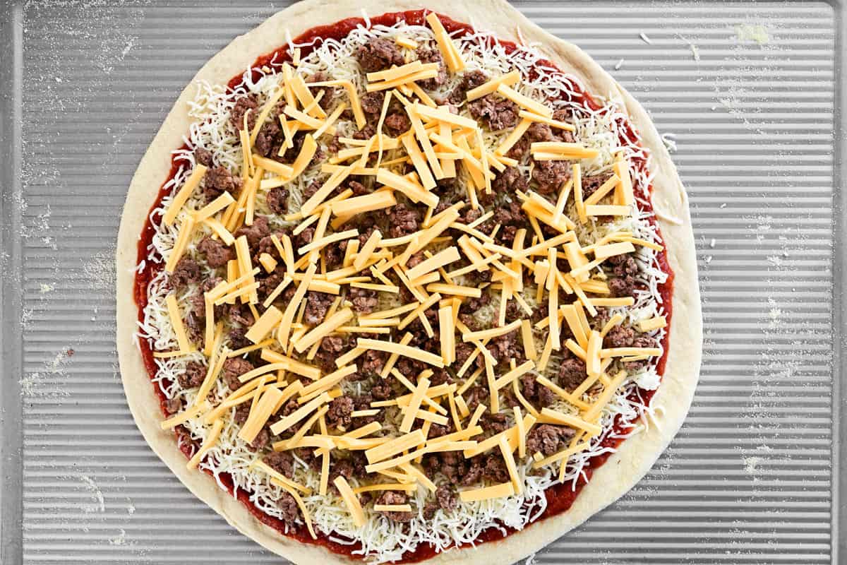 An uncooked pizza with meat and cheese on top.