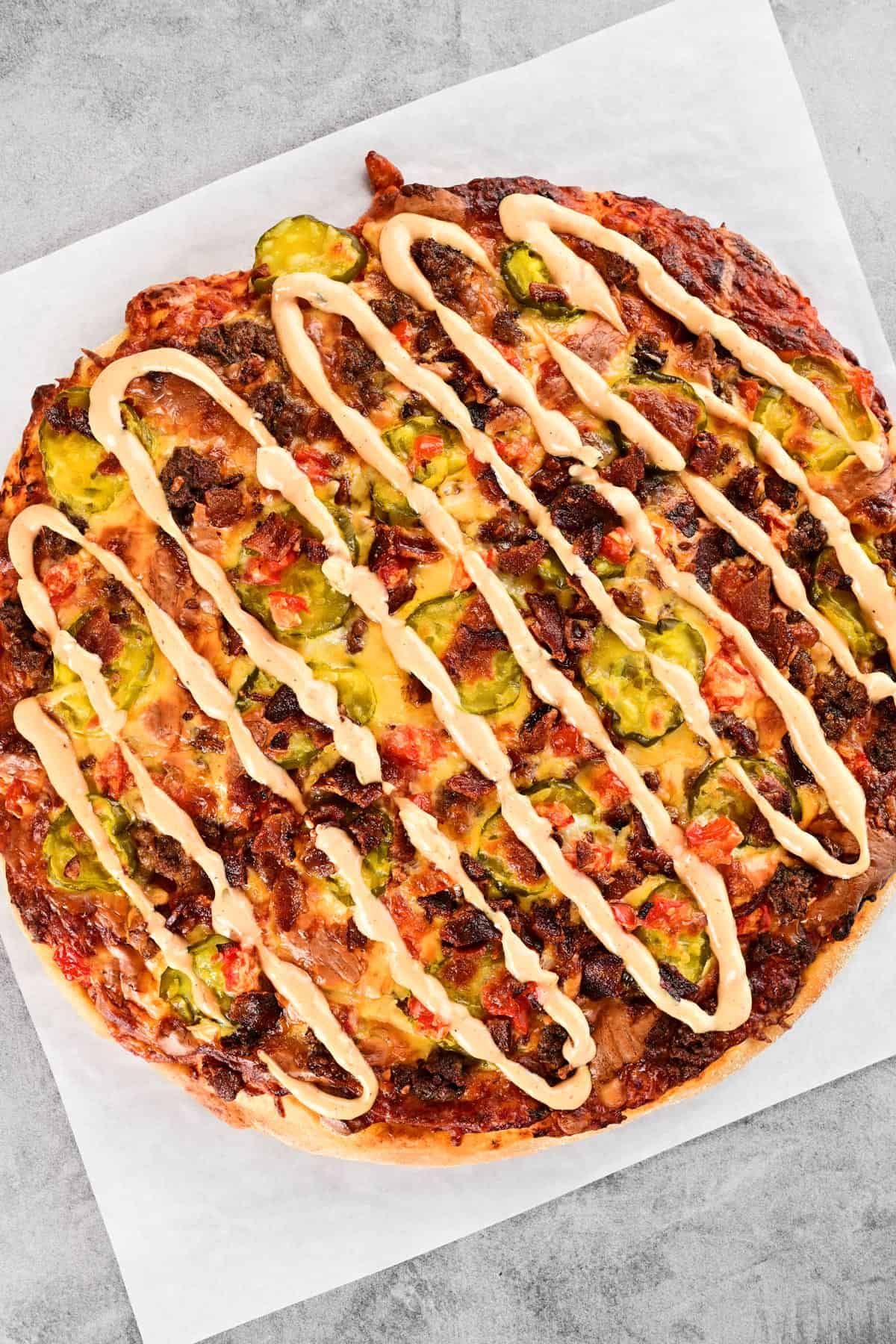 A cheeseburger pizza with burger sauce on top.